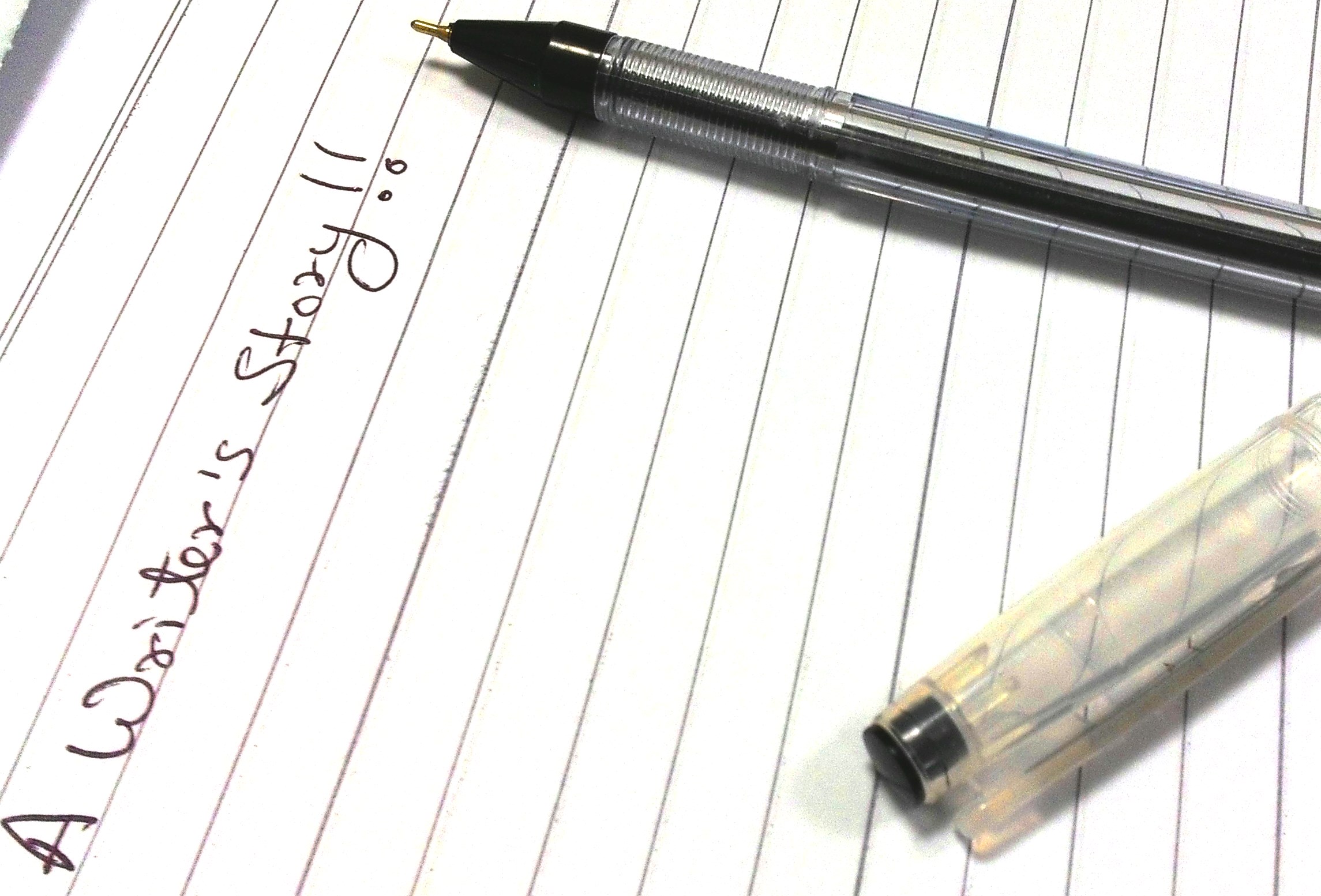 A pad on a desk with a pen resting on it. Some writing reads "A writer's stoy".