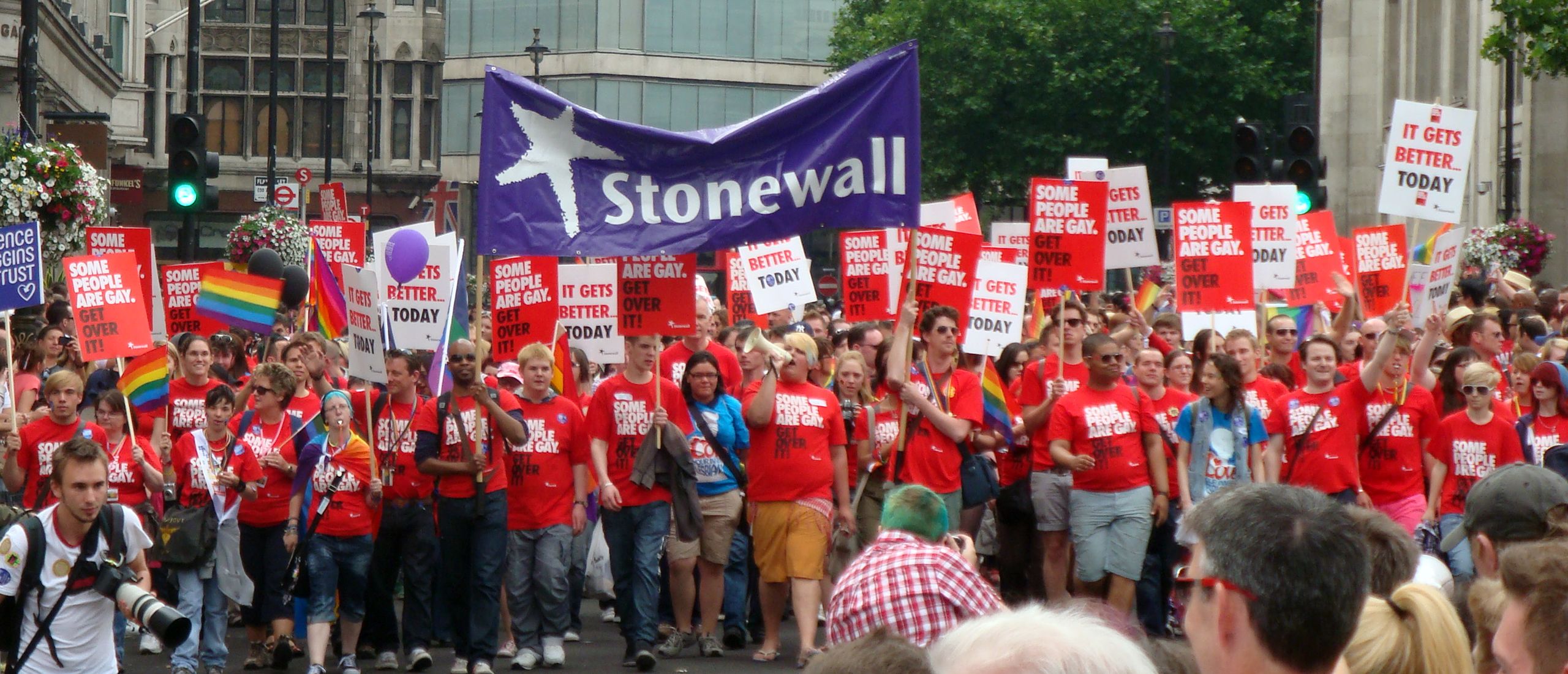 Group photo of activists and campaigners for Stonewall mostly dressed in Stonewall red t-shirts which read phrases such as “Some people are gay, ge...