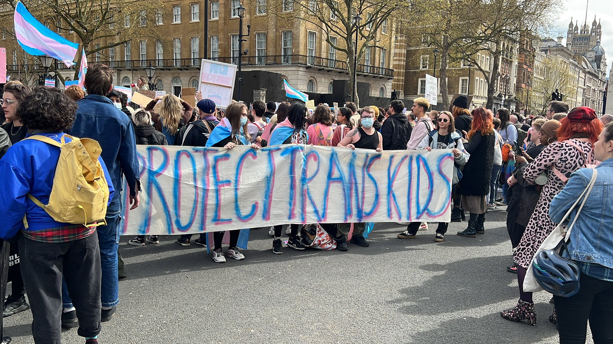 A photo from #BanConversionTherapy Downing Street Protest showing people holding a very long banner reading "protect trans kids".