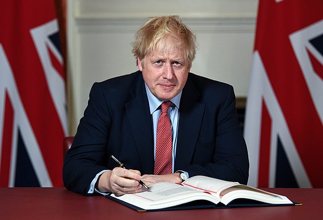 A photo of Boris Johnson with some flags behind him.