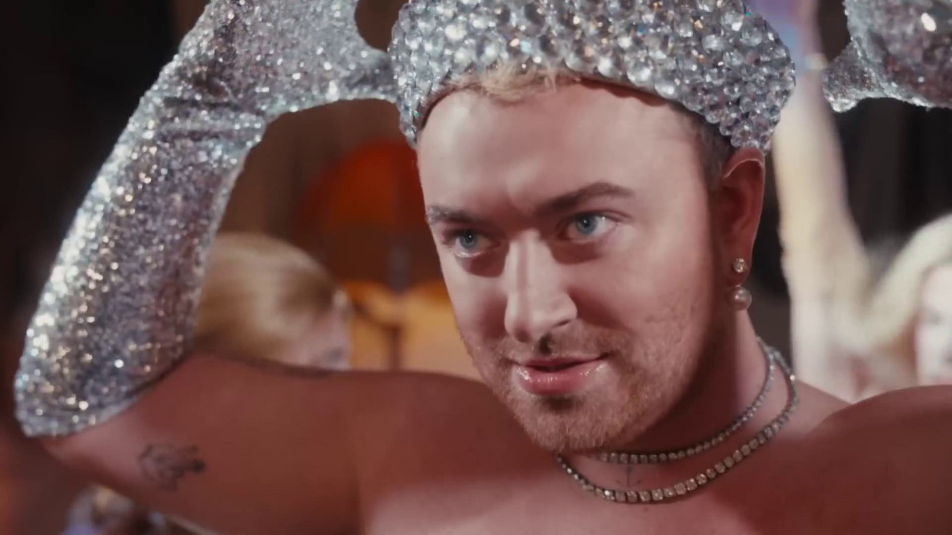 A photo of Sam Smith wearing a bejewelled sailor hat and matching shiny long gloves taken from their video for "I'm Not Here To Make Friends"