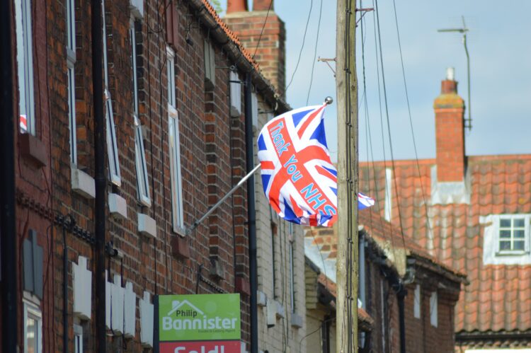 A Union Flag with the words "thank you NHS" written on it limply blows in the wind from a terraced house in the UK. Photocredit Zakhx150 via Wikime...