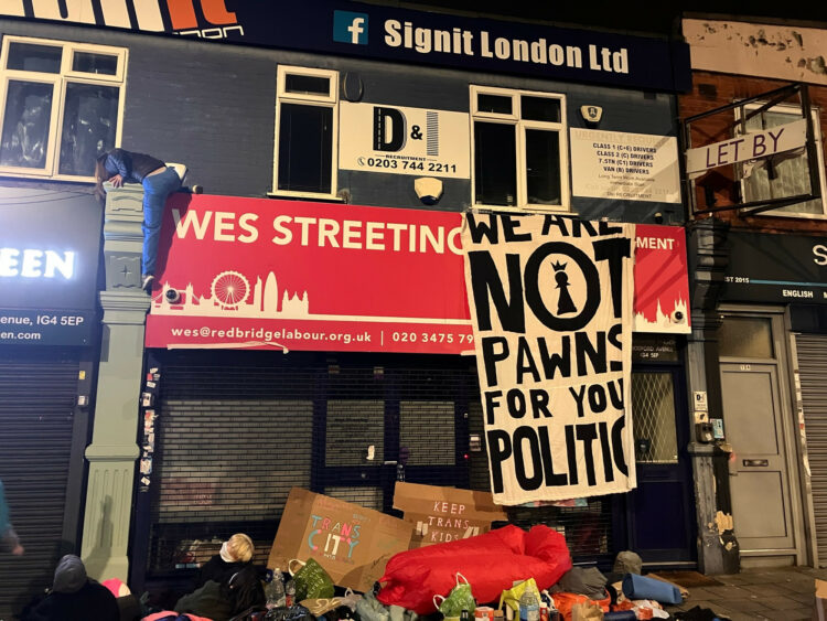 A photo of Wes Streeting's Ilford North constituency office being actively protested by Trans Kids Deserve Better. A large sign hangs from his stor...