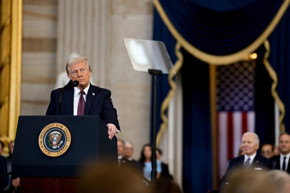 Official White House Photo of Donald Trump at his inauguration as president. He is stood in front of a lectern with the presidential seal and a Uni...