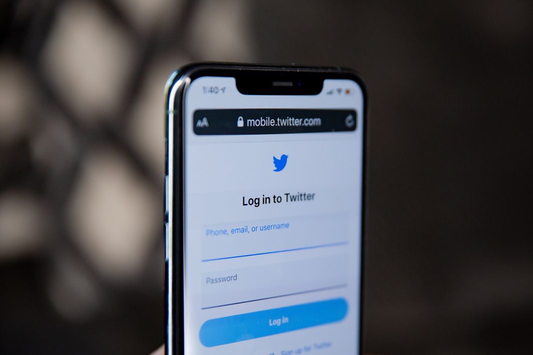 A photo of a phone being held up and showing the Twitter log on screen