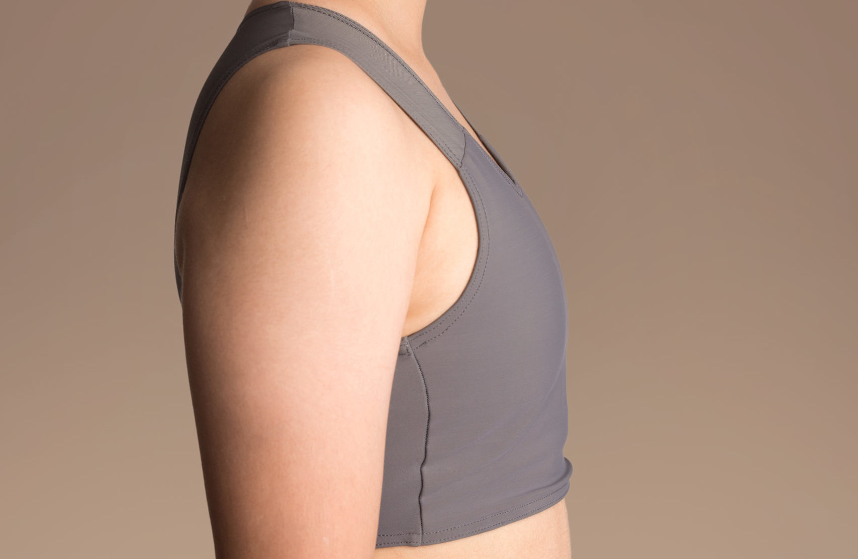 A side profile of someone chest binding with a grey chest binder.