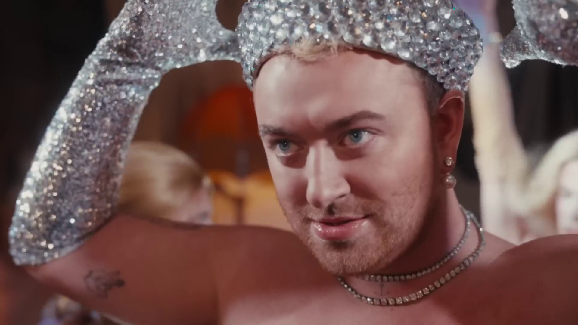 A photo of Sam Smith wearing a bejewelled sailor hat and matching shiny long gloves taken from their video for 