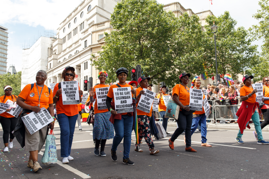 Pride in London 2016's parade showing Ugandan LGBT people marching in orange shirts and holding signs that pay tribute to those who died in the Oralndo terror attack and others which read 