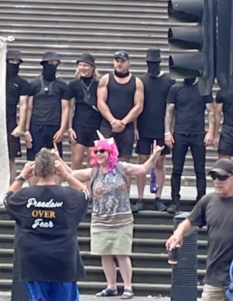 A photo showing an anti-trans attendee of Kellie-Jay Keen's event posing for cameras in front of the group of Nazis who showed up in support of them