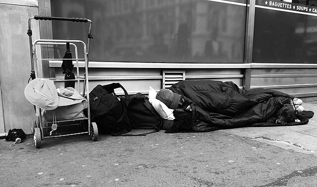  homeless man asleep outside shop. Photo credit Allan Warren [Wikimedia]