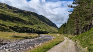 A photo of the trail leading out of the Cairngorms showing mountain on oneside and dense forest on another with river running between the two.